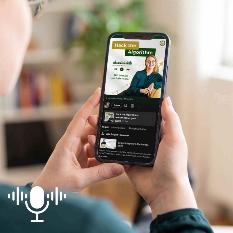Eine Person hält ein Smartphone in beiden Händen. Auf dem Display ist eine Spotify geöffnet, die den Kanal "Hack the Algorithm – SEO Podcast mit Julia Hacker" anzeigt. Auf dem Bildschirm ist das Coverbild mit Julia Hacker in einer grünen Bluse sowie eine aktuelle Episode zum Thema Keyword-Recherche zu sehen.