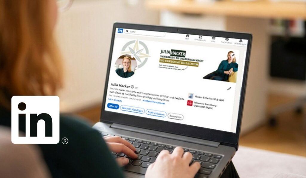Eine Frau mit rötlichen Haaren sitzt von hinten im Anschnitt auf einem Sessel und tippt auf einem grauen Laptop. Der Bildschirm zeigt das LinkedIn Profil von Julia Hacker